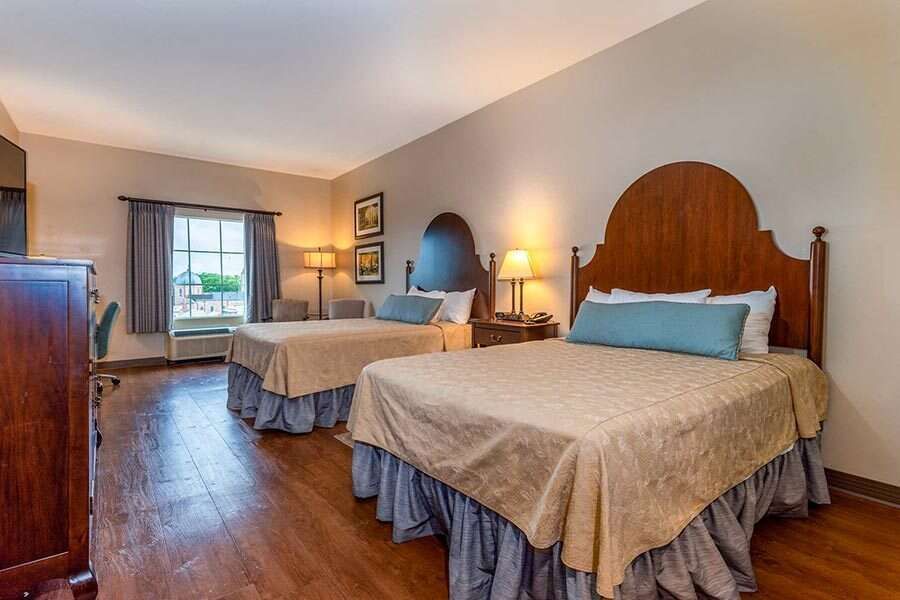 Hotel room with two beds, wooden headboards, and a window with curtains.