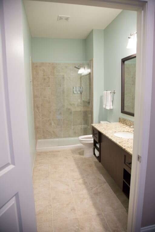 Bathroom with blue walls, tan tile floors, sink, toilet, and shower.
