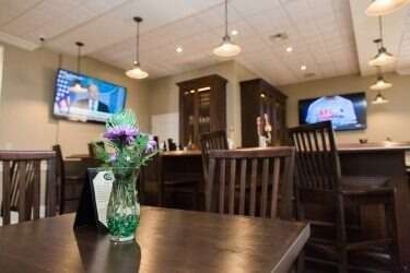 A bar with wooden tables and chairs, two TVs, and hanging lights.