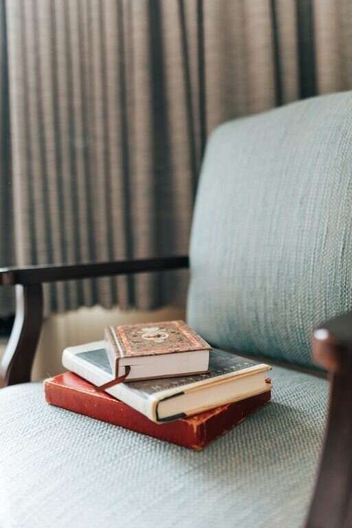Three books stacked on a light blue armchair, near a window with gray curtains.