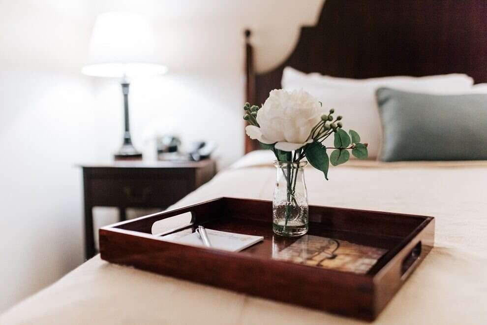 Wooden tray on bed with white flowers, lamp, and nightstand in a bedroom.