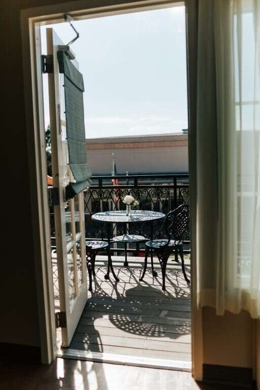 Open doorway to a balcony with a table and chairs. Bright sunlight and shadows.