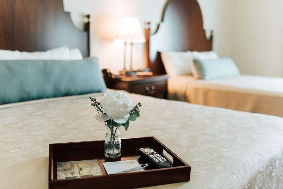 Two hotel beds with floral arrangement and remote on a tray.