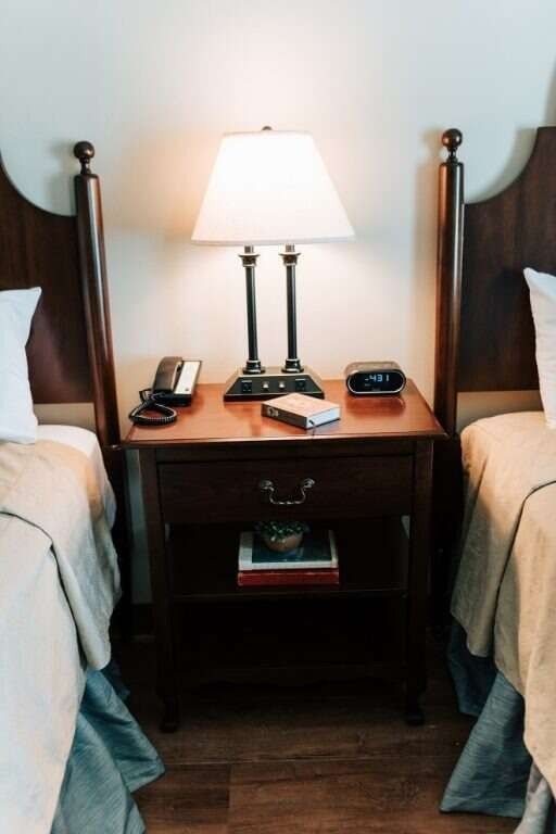 Two twin beds with dark wood headboards flank a nightstand with a lamp, phone, and alarm clock.