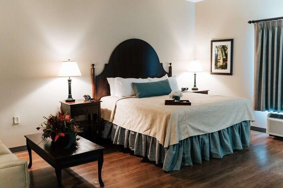 Bedroom with a king-sized bed, two lamps, a dark wood nightstand, a table, and a framed picture.