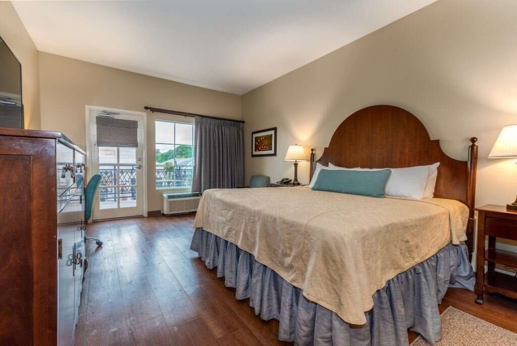 Bedroom with king-size bed, desk, balcony access. Earth tones, wooden furniture, natural light.