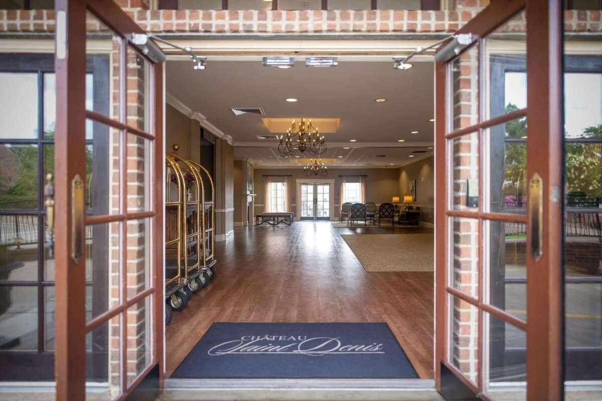 Hotel entrance: Open glass doors reveal a spacious lobby with chandeliers, luggage carts, and a welcome mat.
