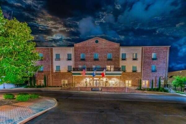 Hotel exterior at night with brick facade, illuminated entrance, flags, and dark sky.