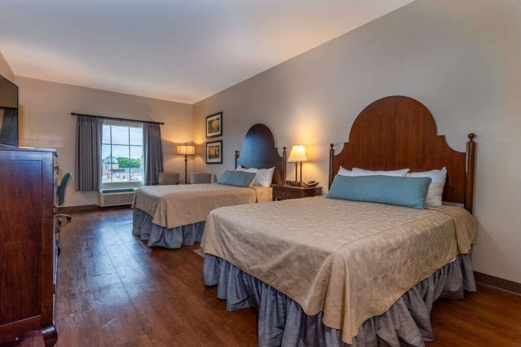 A hotel room with two double beds, wooden floors, and a window with gray curtains.