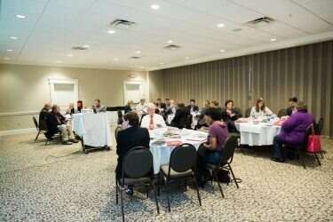 People in a conference room seated at round tables, discussing a topic.