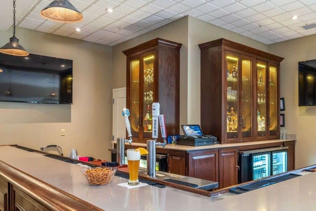 A bar with a light-colored counter, wooden cabinets with liquor, beer taps, and a TV on the wall.
