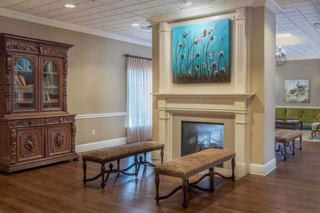 Ornate living room with fireplace, benches, and large antique cabinet. Blue artwork hangs above fireplace.